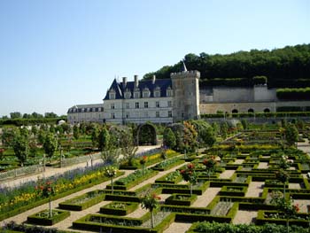 Castillo francés con jardines geométricos y colinas arboladas al fondo en un día claro