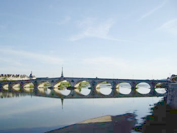 Puente de piedra con arcos reflejados en el río Loira en un día soleado